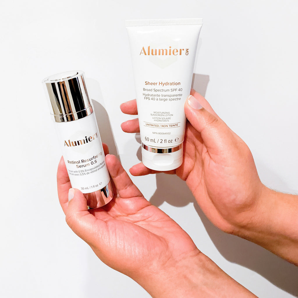 Hands holding Alumier Sheer Hydration Bottle in the right hand and Retinol Resurfacing Serum 0.5 in the left hand in front of a white backdrop.